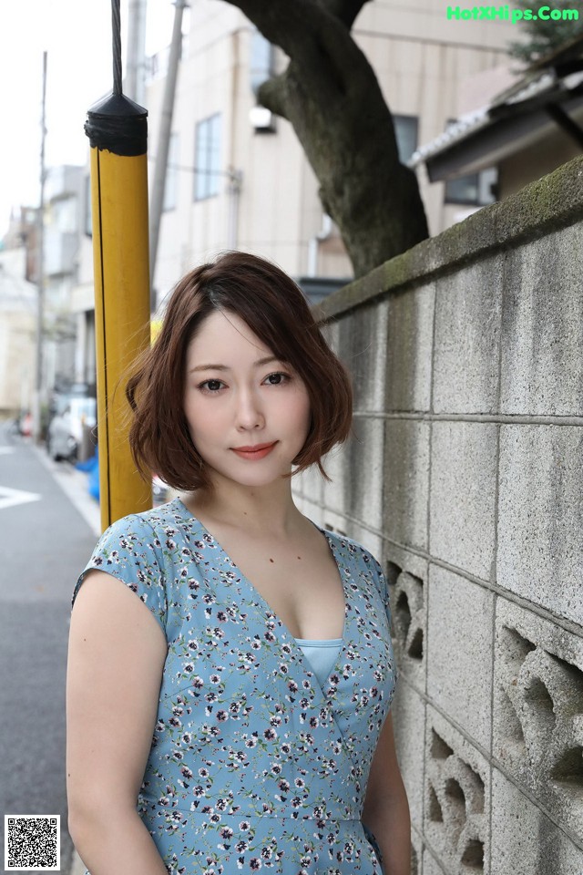 A woman in a blue dress leaning against a wall.